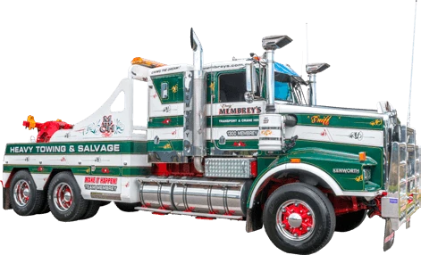 A large green and white tow truck with red wheel rims, chrome accents, and "Heavy Towing & Salvage" written on the side. The truck is branded with "Membrey's" and has industrial equipment attached.
