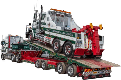 A large tow truck is being transported on a flatbed trailer pulled by another heavy-duty truck. The vehicles are designed for heavy towing and salvage work, with visible branding and equipment.